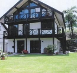 A modern house with a black facade and large windows. The well-maintained garden is designed with lawn and plants.
