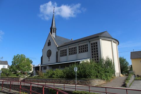 Eine elegante Kirche mit einem hohen Turm und großen Fenstern. Sie steht in einer ruhigen Umgebung unter einem blauen Himmel.