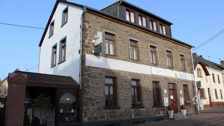 Ein historisches Gebäude mit Steinfassade, Fenstern und einem Schild. Es liegt an einer Straße und hat eine einladende Atmosphäre.