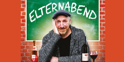 A man is sitting in front of a board with the inscription "Parent-Teacher Meeting." Next to him are bottles of wine and a casual atmosphere is palpable.