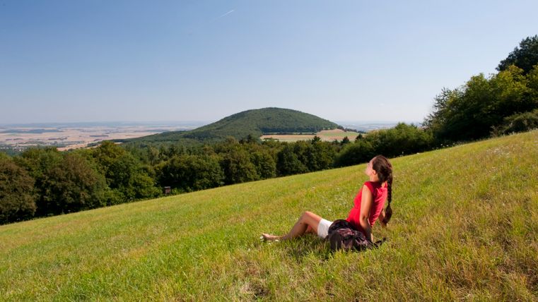 Eine Frau sitzt auf einer Wiese und blickt auf den bewaldeten Hochsimmer.
