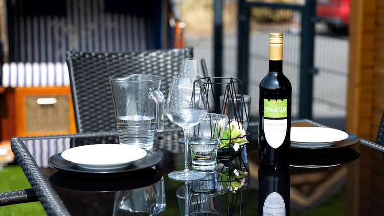 A beautifully set table outdoors with a wine bottle, glasses, and plates. The atmosphere feels inviting and relaxed.