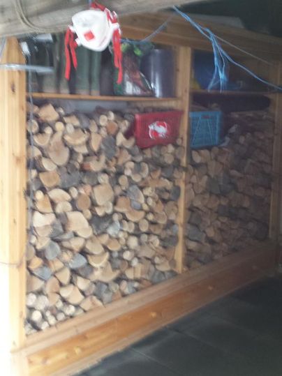 Ein Holzlager aus Kiefernholz, ordentlich gestapelt in einem Holzregal. Darüber befinden sich einige kleinere Behälter und Dekoration.