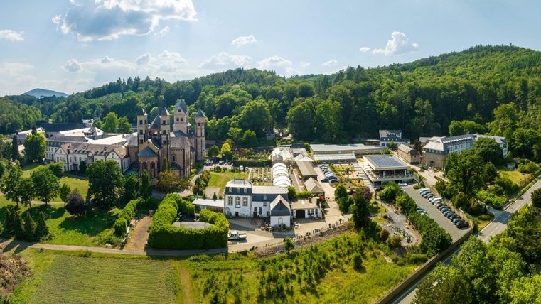 Eine malerische Landschaft mit einem historischen Gebäude und grünen Wäldern im Hintergrund. Die Anlage ist von Weinbergen umgeben, was eine idyllische Atmosphäre schafft.