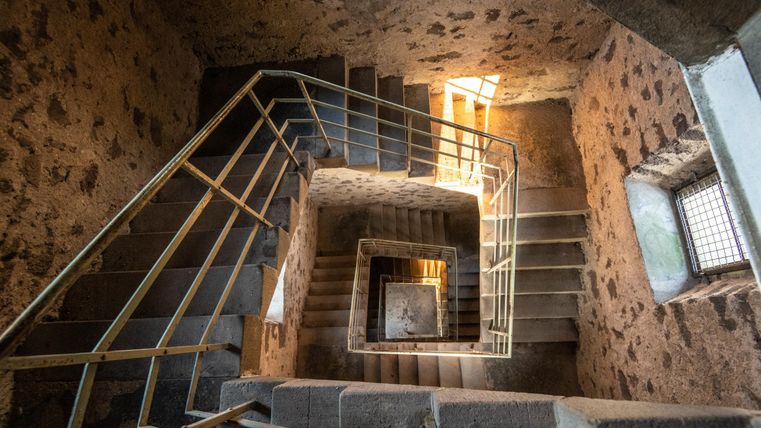 A simple, spiral staircase made of concrete and stone. Light streams through a window at the end of the staircase.