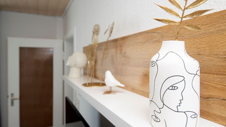 Eine moderne Wohnungsecke mit einer dekorativen Vase und minimalistischen Figuren auf einem Regal. Die Kombination aus Holz und hellen Farben schafft eine angenehme Atmosphäre.