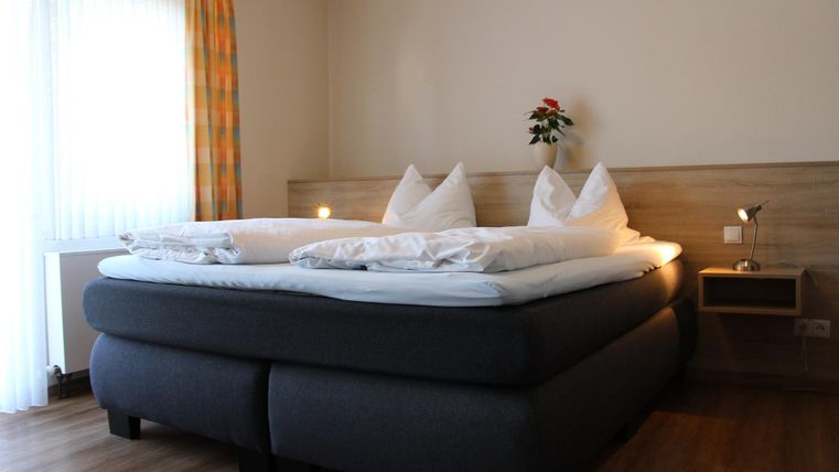 Ein gemütliches Schlafzimmer mit einem großen Doppelbett und dekorativen Kopfkissen. Das Fenster lässt viel Tageslicht herein und sorgt für eine einladende Atmosphäre.