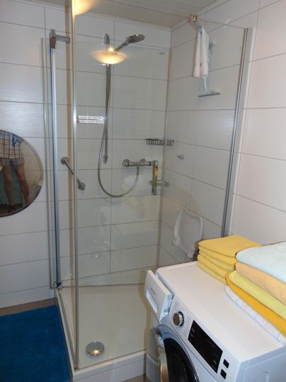 A modern bathroom with a shower and a washing machine. On a shelf lie yellow and green towels.