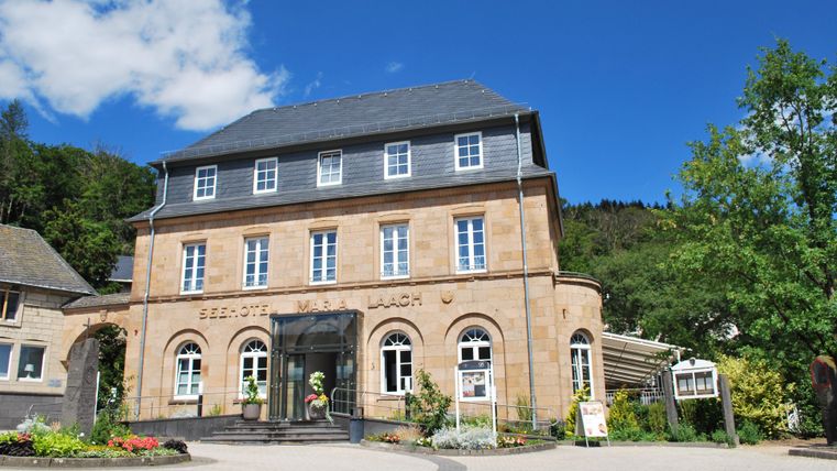 Ein historisches Gebäude mit einer eleganten Fassade und großen Fenstern. Umgeben von grünen Bäumen und gepflegten Blumenbeeten.