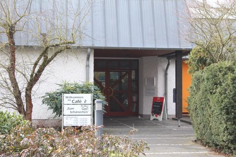 An inviting entrance to a café with a modern facade. Surrounded by bushes and trees, the environment feels friendly and cozy.