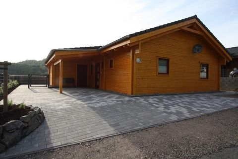 Ein modernes Holzhaus mit einer hellen Fassade. Der Eingangsbereich ist mit grauen Steinen gepflastert und es gibt einen Ausblick auf die umgebende Landschaft.