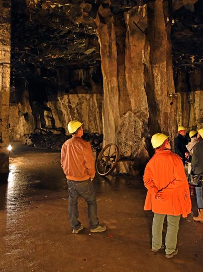 Eine Gruppe von Personen in einem Bergwerk, die harte Hüte tragen. Sie stehen vor großen Felsformationen und besichtigen den unterirdischen Raum.