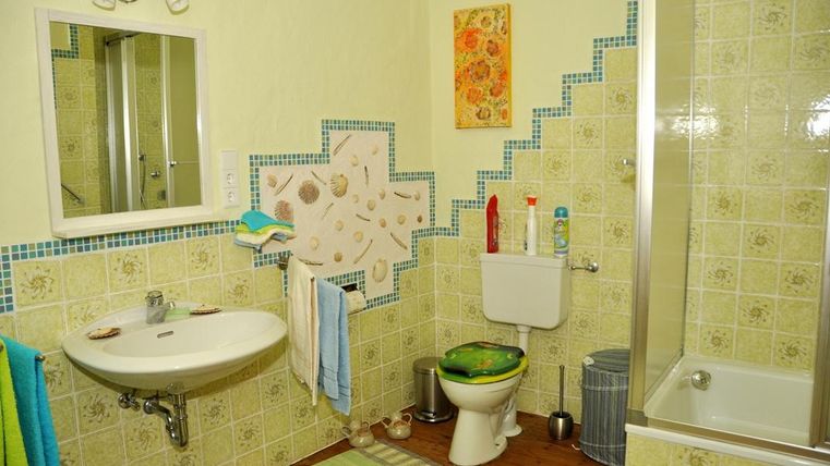 Ein helles Badezimmer mit einer Dusche, einem Waschbecken und einer Toilette. Die Wände sind mit bunten Fliesen und einem dekorativen Bild gestaltet.