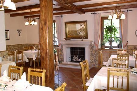 Ein gemütliches Restaurant mit Holzdecken und warmem Licht. Tische sind festlich gedeckt und ein Kamin sorgt für eine einladende Atmosphäre.