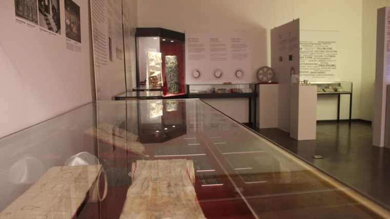 Ein Innenraum eines Museums mit einem Ausstellungstisch und verschiedenen Objekten. An den Wänden sind Informationsgrafiken und Beschreibungen angebracht.