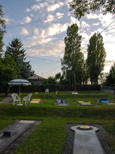 Ein gepflegter Minigolfplatz mit verschiedenen Bahnen und grünem Rasen. Im Hintergrund sind Bäume und ein sonniger Himmel zu sehen.