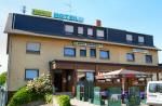 Ein Hotel mit mehreren Fenstern und einem Eingang. Vor dem Gebäude gibt es eine Terrasse mit Tischen und Stühlen.