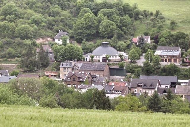 A picturesque landscape with a small village surrounded by green trees. In the center stands a large, round building that catches the eye.