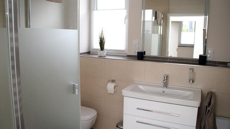 Ein modernes Badezimmer mit einer Glasdusche und einem hellen Waschbecken. Es hat große Spiegel und eine dezente Pflanze für eine frische Atmosphäre.