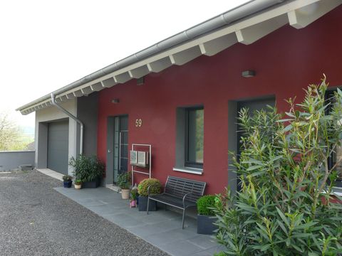 Ein modernes Haus mit roter Fassade und einem grünen Vorgarten. Eine Sitzgelegenheit aus Holz steht vor dem Eingang.