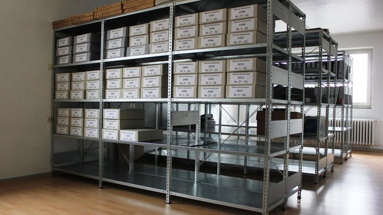 A room with high shelves filled with labeled boxes. The floor is made of wood, and the room appears tidy and structured.