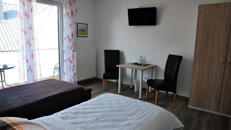 Ein gemütliches Schlafzimmer mit zwei Betten, einem Tisch und Stühlen. Es gibt ein Fenster mit Zugang zum Balkon und einen Fernseher an der Wand.