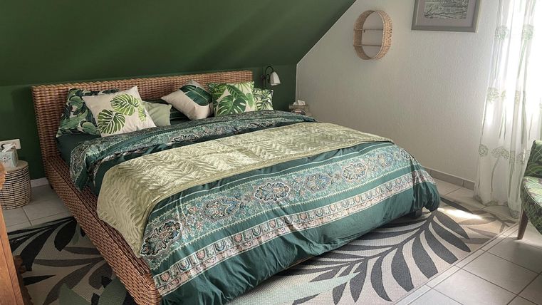 Ein stilvolles Schlafzimmer mit einem großen Bett und grüner Bettwäsche. Die Wände sind grün gestrichen und die Raumgestaltung ist harmonisch und einladend.