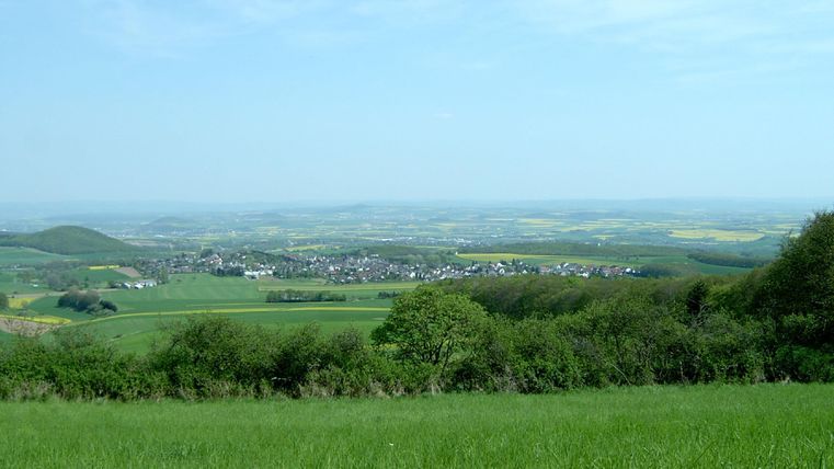 Ein weites, grünes Tal mit sanften Hügeln und verstreuten Dörfern. Der Himmel ist klar und blau.