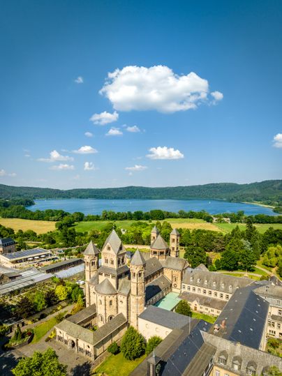 Eine beeindruckende Architektur steht an einem malerischen Seeufer. Im Hintergrund sind sanfte Hügel und ein strahlend blauer Himmel mit einigen Wolken zu sehen.