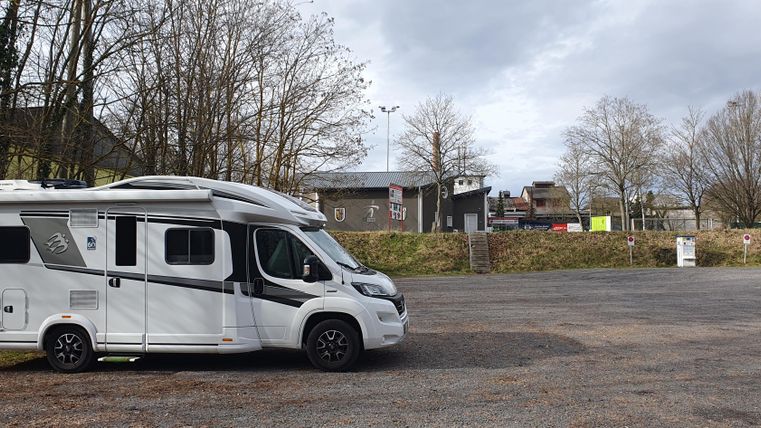 A motorhome is parked in a quiet parking lot. In the background, there are a few trees and buildings visible.
