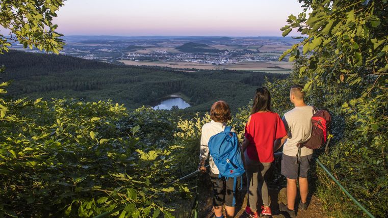 Eine Gruppe von Wanderern steht an einem Aussichtspunkt und blickt auf eine malerische Landschaft. Im Hintergrund sind sanfte Hügel und ein klarer Himmel zu sehen.