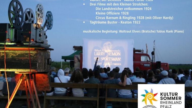 Ein Freiluftkino mit einem Filmvorführungsprojektor und einer sitzenden Menge von Zuschauern. Im Hintergrund sind Bäume und ein Lkw zu sehen, während auf einer Leinwand alte Filme gezeigt werden.