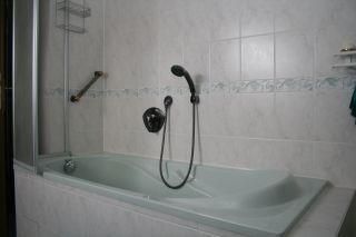 Eine moderne Badezimmeransicht mit einer Badewanne und einer Dusche. Die Wände sind hell gefliest und das Design ist funktional.