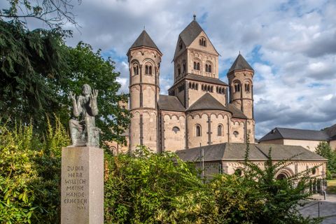 Eine beeindruckende Kirche mit markanten Türmen und einem historischen Steinbau. Im Vordergrund steht eine Statue, die Aufmerksamkeit auf die Umgebung lenkt.