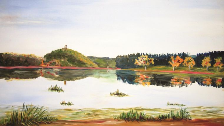 Eine ruhige Landschaft mit einem See und sanften Hügeln im Hintergrund. Bunte Bäume reflektieren sich im Wasser, das eine friedliche Atmosphäre schafft.