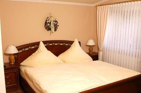 Ein gemütliches Schlafzimmer mit einem großen Bett und zwei dekorativen Kissen. Weiche Vorhänge und Nachtlichter verleihen dem Raum eine wohnliche Atmosphäre.