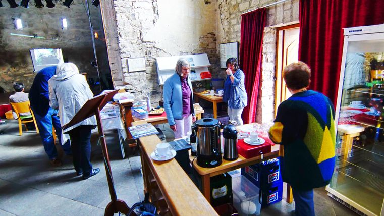 Ein gemütlicher Innenraum mit mehreren Personen. Es gibt Tische, eine Kaffeemaschine und eine Kühlschrankanordnung, um Getränke anzubieten.