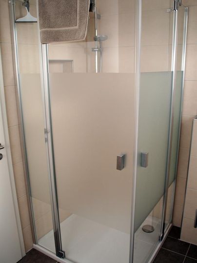 Eine moderne Dusche mit Glaswänden und einem Handtuch. Der Duschbereich ist elegant und hell gestaltet.