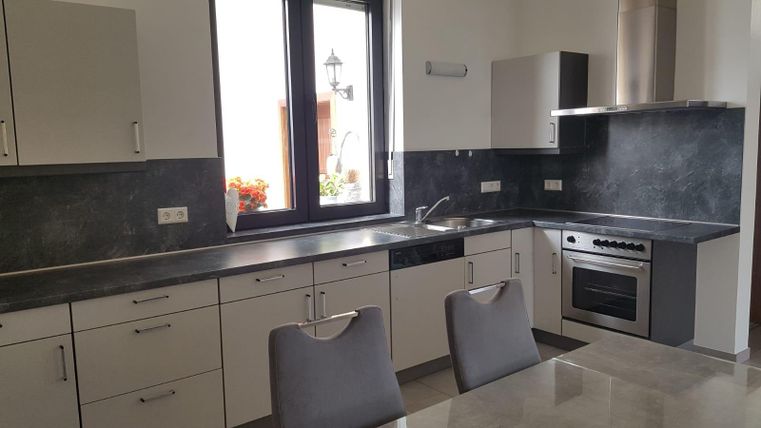 A modern kitchen with light cabinets and a dark countertop. Large windows provide plenty of light and an inviting atmosphere.