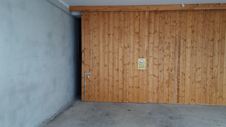 Eine Garagentür aus Holz mit einem Warnschild. Der Raum ist leer und hat eine graue Wand.