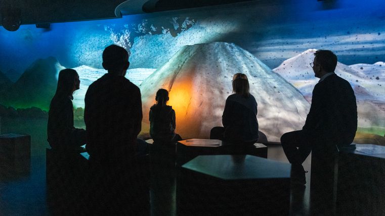 Personen sitzen vor einer beleuchteten Vulkanprojektion im Lava-Dome Mendig.