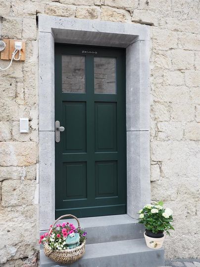 Eine elegante grüne Tür mit großen Fenstern in einem Steinmauerrahmen. Vor der Tür steht ein Blumentopf mit bunten Blumen.