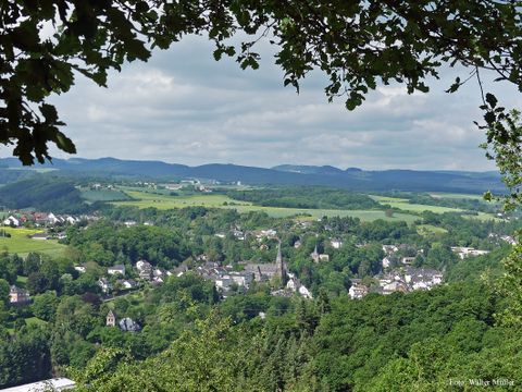 Panoramablick auf Burgbrohl mit Kirche im Zentrum, umgeben von grüner Landschaft und Hügeln.