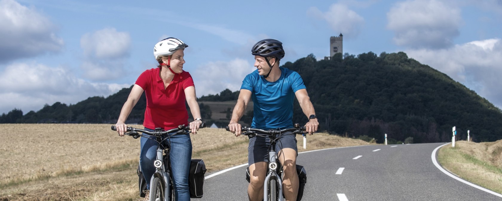 Zwei Fahrradfahrer fahren eine Stra&szlig;e entlang. Im Hintergrund die Burg Olbr&uuml;ck., &copy; Vulkanregion Laacher See, Klaus-Peter Kappest