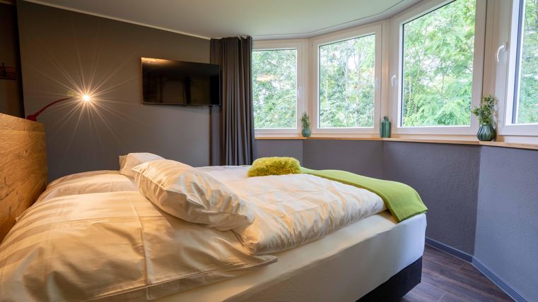 Ein modernes Schlafzimmer mit einem großen Fenster und Blick ins Grüne. Die Betten sind gemütlich und mit hellen Kissen dekoriert.