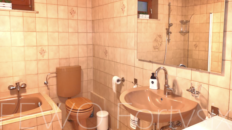 A simple bathroom with tiled walls, a bathtub, a sink, and a toilet. The light is warm and the decor feels functional.