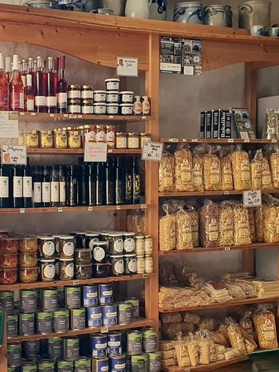 A well-organized store with various foods and drinks. The shelves are filled with jam, oil, pasta, and other products.