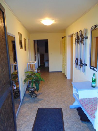 A bright hallway with friendly colors and a carpet. On the left side, there are plants and a coat rack.