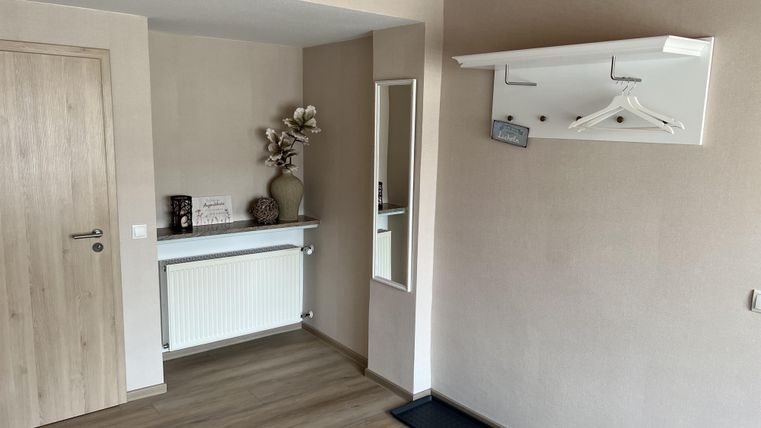 Ein heller Flur mit einer Garderobe und einem kleinen Spiegel. An der Wand hängt ein Regal mit Kleiderhaken und einer Vase.