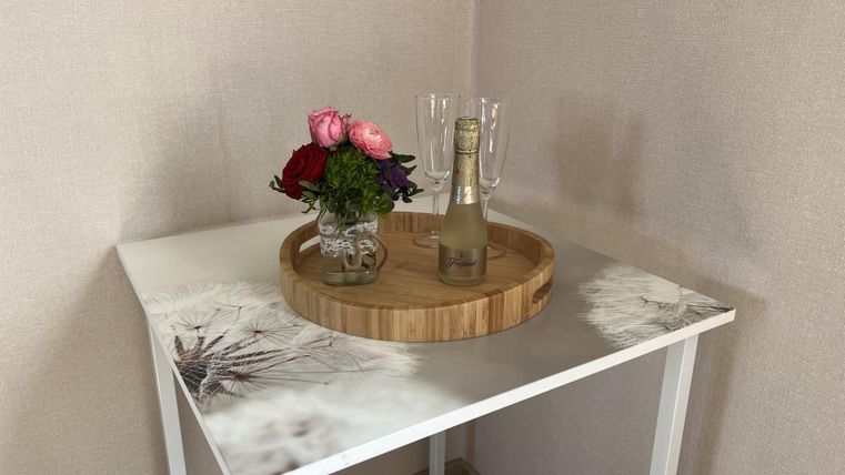 Ein kleiner Tisch mit einer Holzkugel und einem Blumenstrauß. Auf dem Tisch stehen auch Sektgläser, bereit für eine Feier.